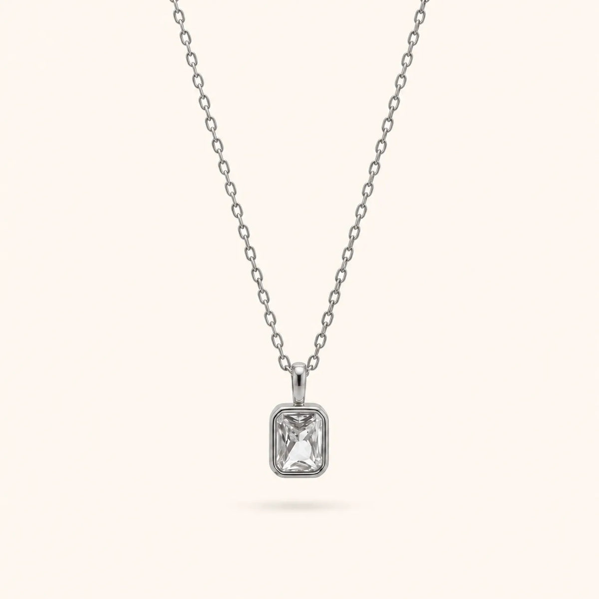 A silver chain necklace with a rectangular bezel-set clear gemstone pendant, shown against a solid off-white background.