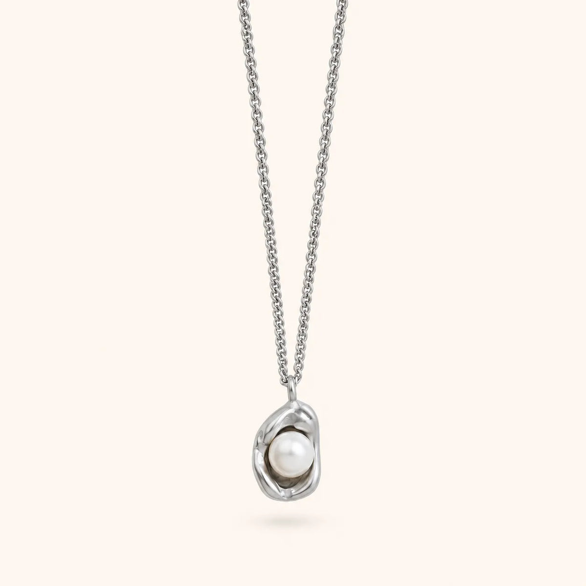 A silver chain necklace with an abstract, organic-shaped silver pendant holding a single white pearl, shown against a solid pale cream background.