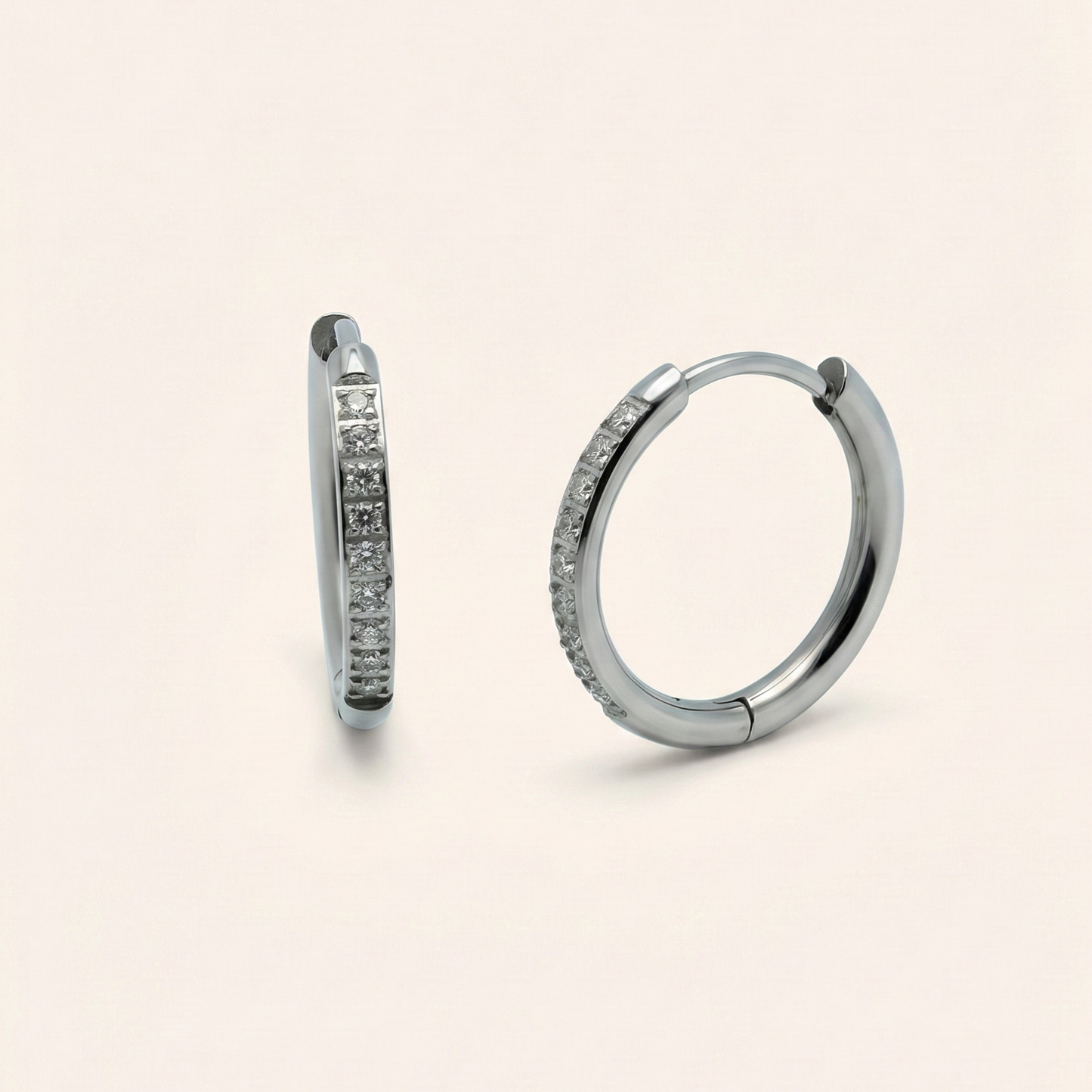 Pair of silver hoop earrings with embedded stones on a beige background