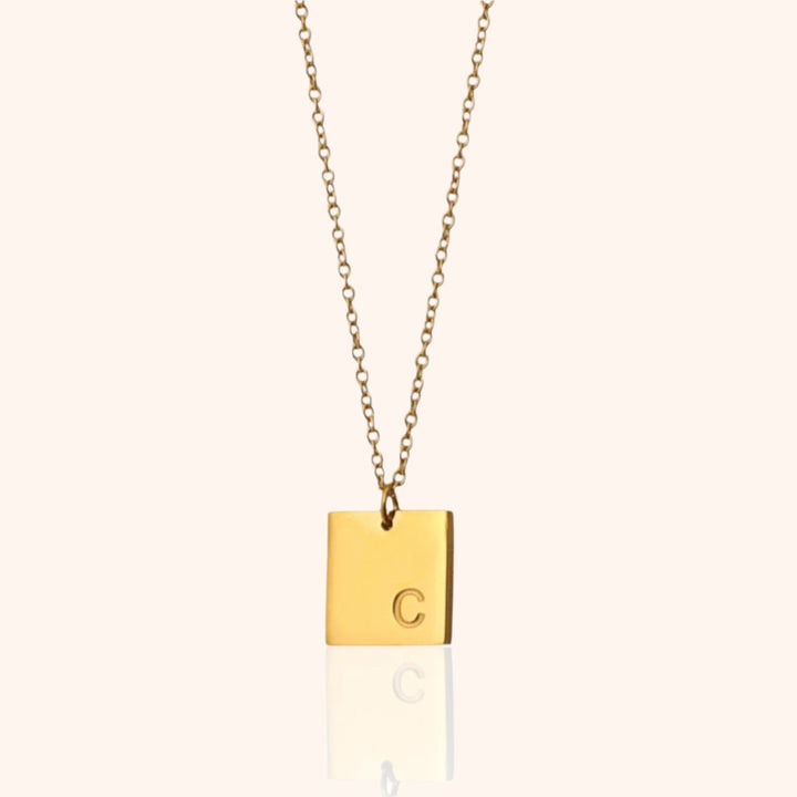 Close-up of a gold square pendant necklace with the initial "C" engraved, showcasing its personalized design.