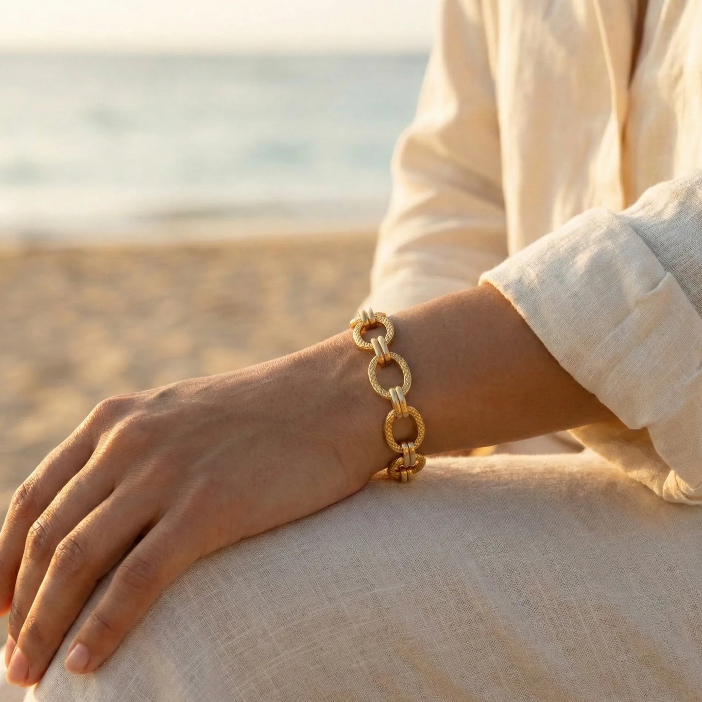 Gold chain bracelet on a wrist with a blurred beach background