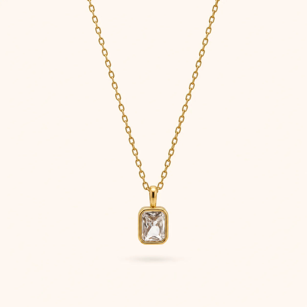 A delicate gold chain necklace with a rectangular bezel-set clear gemstone pendant, shown against a solid off-white background.