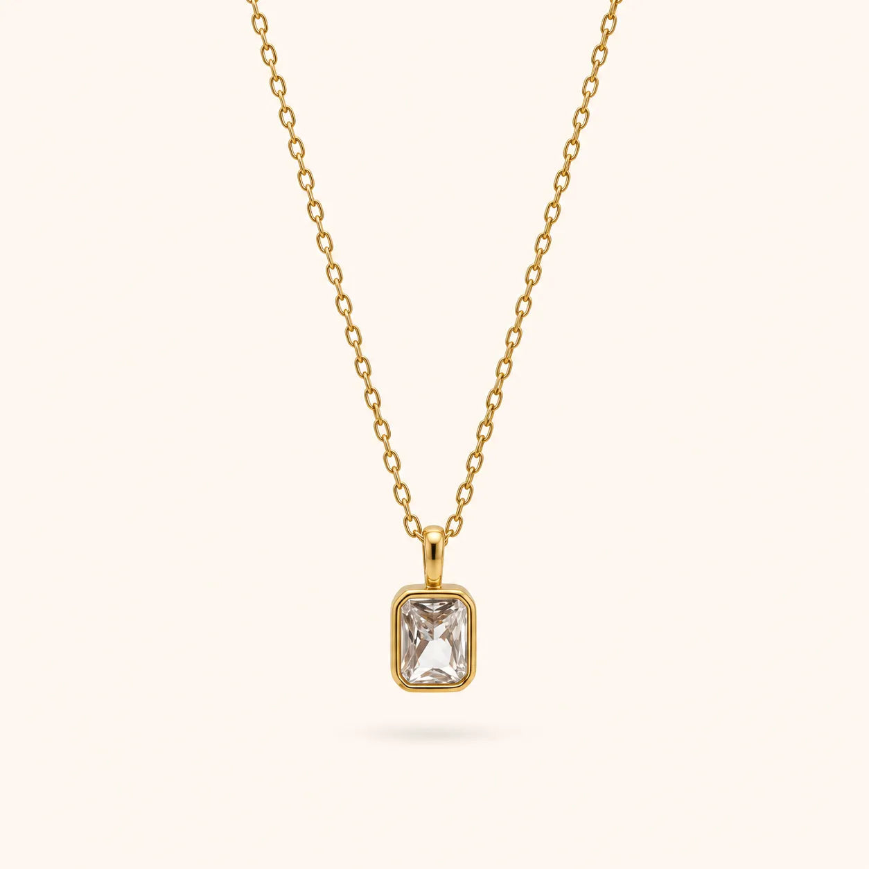 A delicate gold chain necklace with a rectangular bezel-set clear gemstone pendant, shown against a solid off-white background.