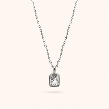 A silver chain necklace with a rectangular bezel-set clear gemstone pendant, shown against a solid off-white background.