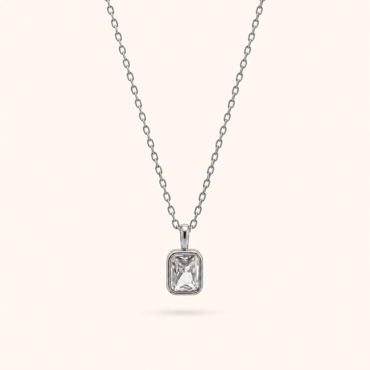 A silver chain necklace with a rectangular bezel-set clear gemstone pendant, shown against a solid off-white background.