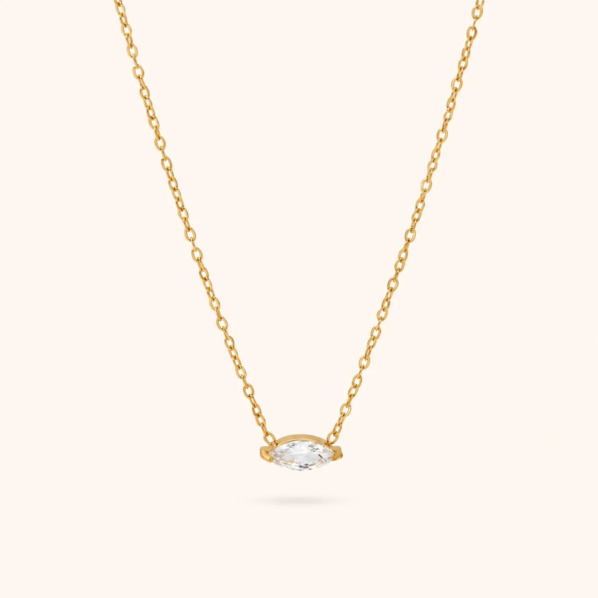 A delicate yellow gold chain necklace featuring a small marquise-cut clear gemstone pendant in a gold bezel setting, shown against a solid off-white background.