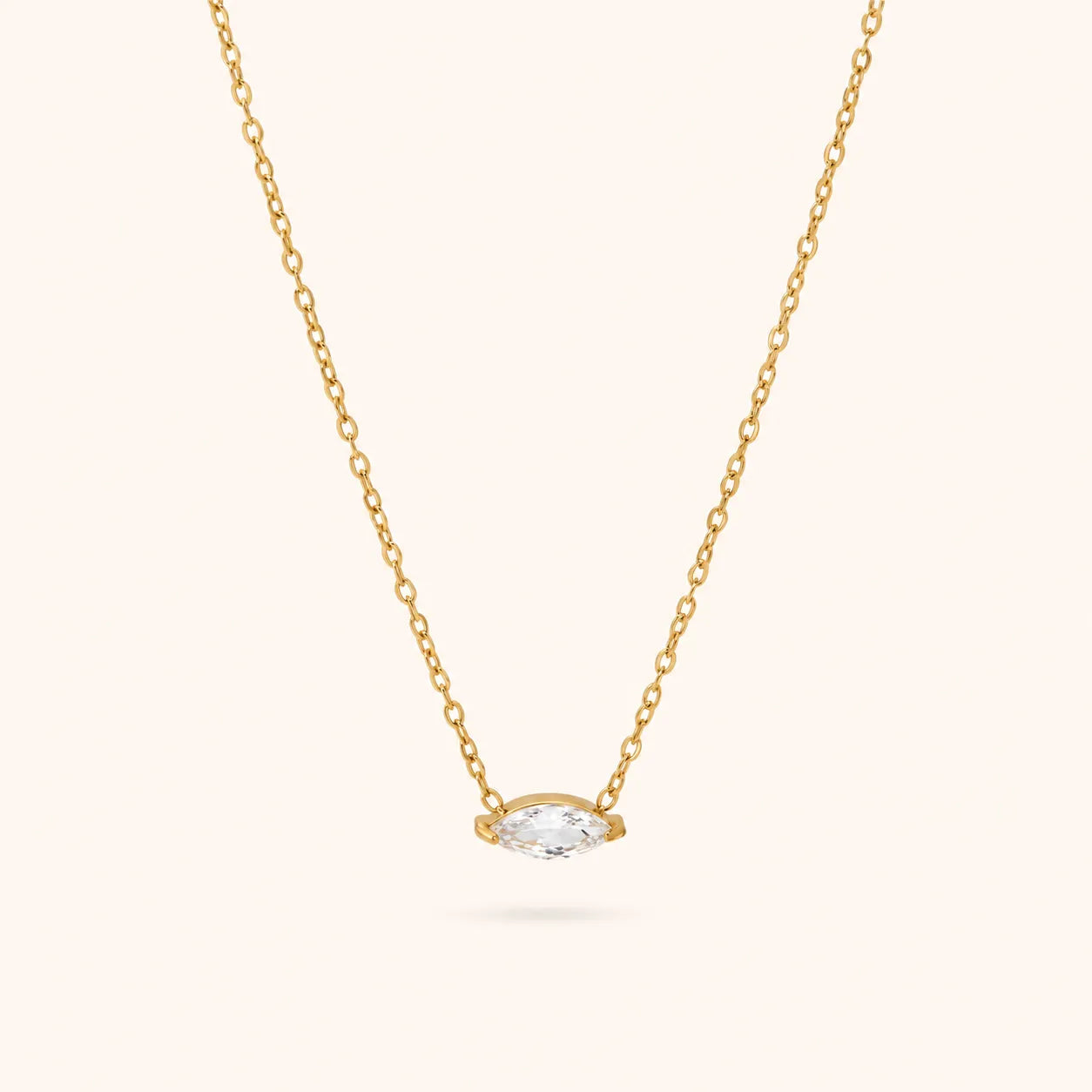 A delicate yellow gold chain necklace featuring a small marquise-cut clear gemstone pendant in a gold bezel setting, shown against a solid off-white background.