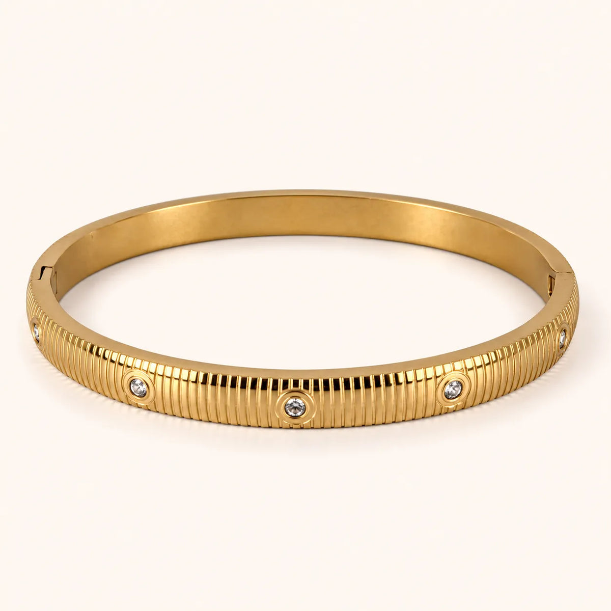 A gold bangle bracelet with a ribbed textured exterior and three small round clear stones set into the band, photographed on a clean off-white background.