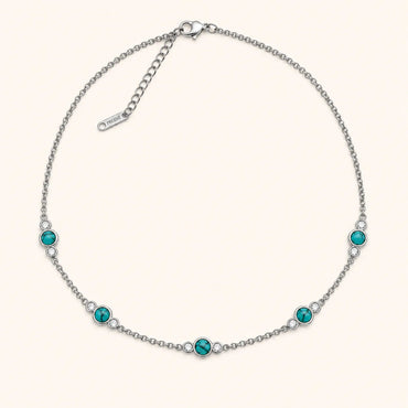 A silver chain necklace with five evenly spaced round turquoise-blue gemstones, each accented with a small clear crystal, on a light cream background.