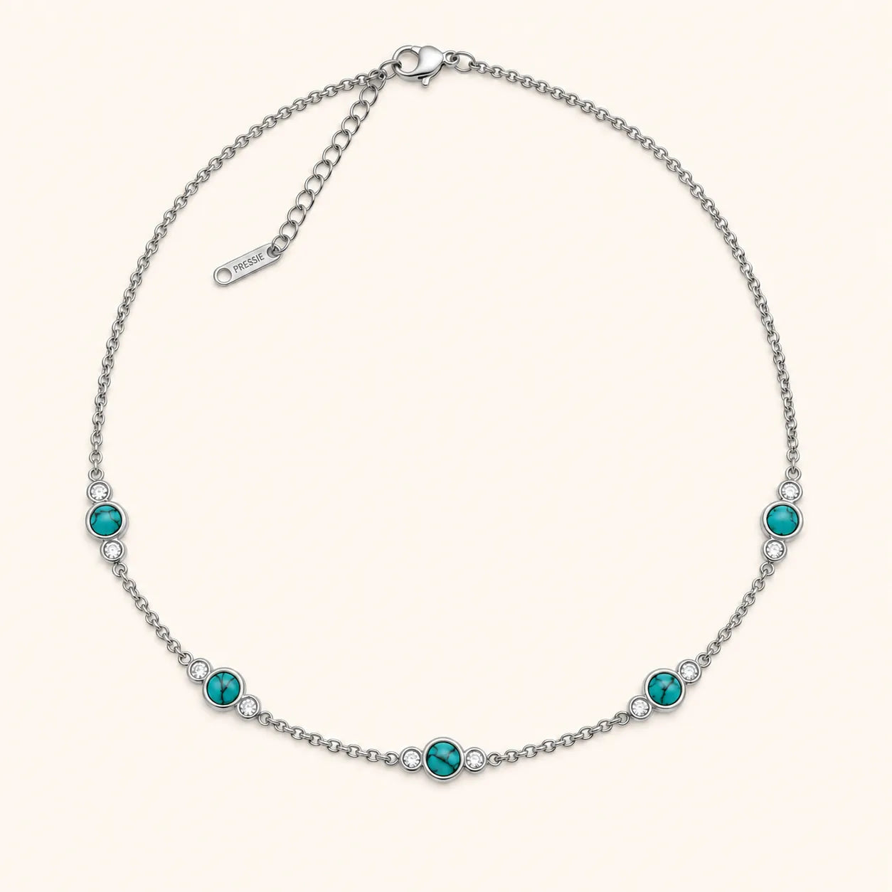 A silver chain necklace with five evenly spaced round turquoise-blue gemstones, each accented with a small clear crystal, on a light cream background.