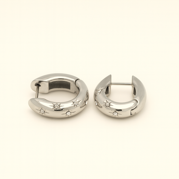 Pair of silver hoop earrings with star and gemstone details on a light beige background