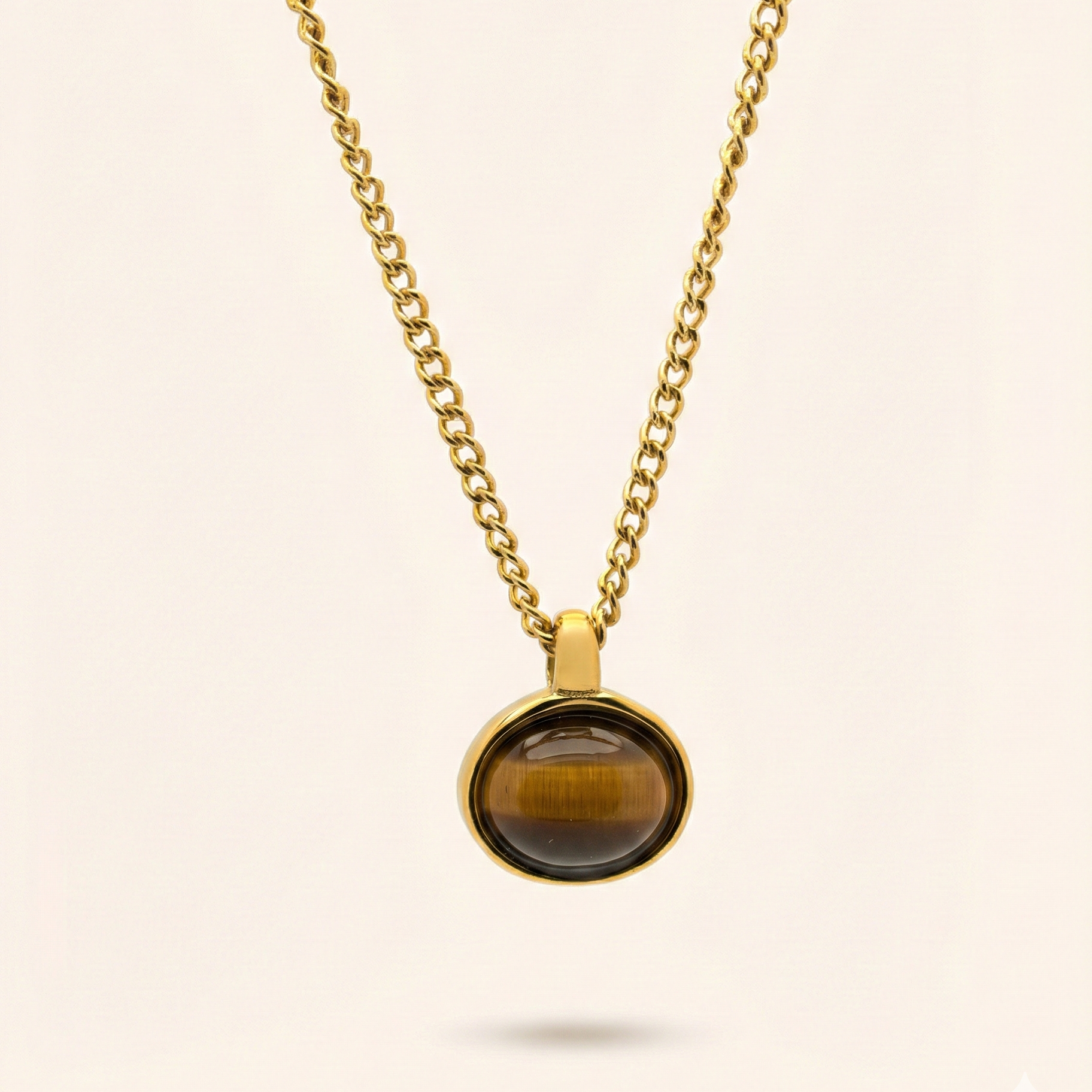 Gold necklace with a tiger's eye pendant on a beige background