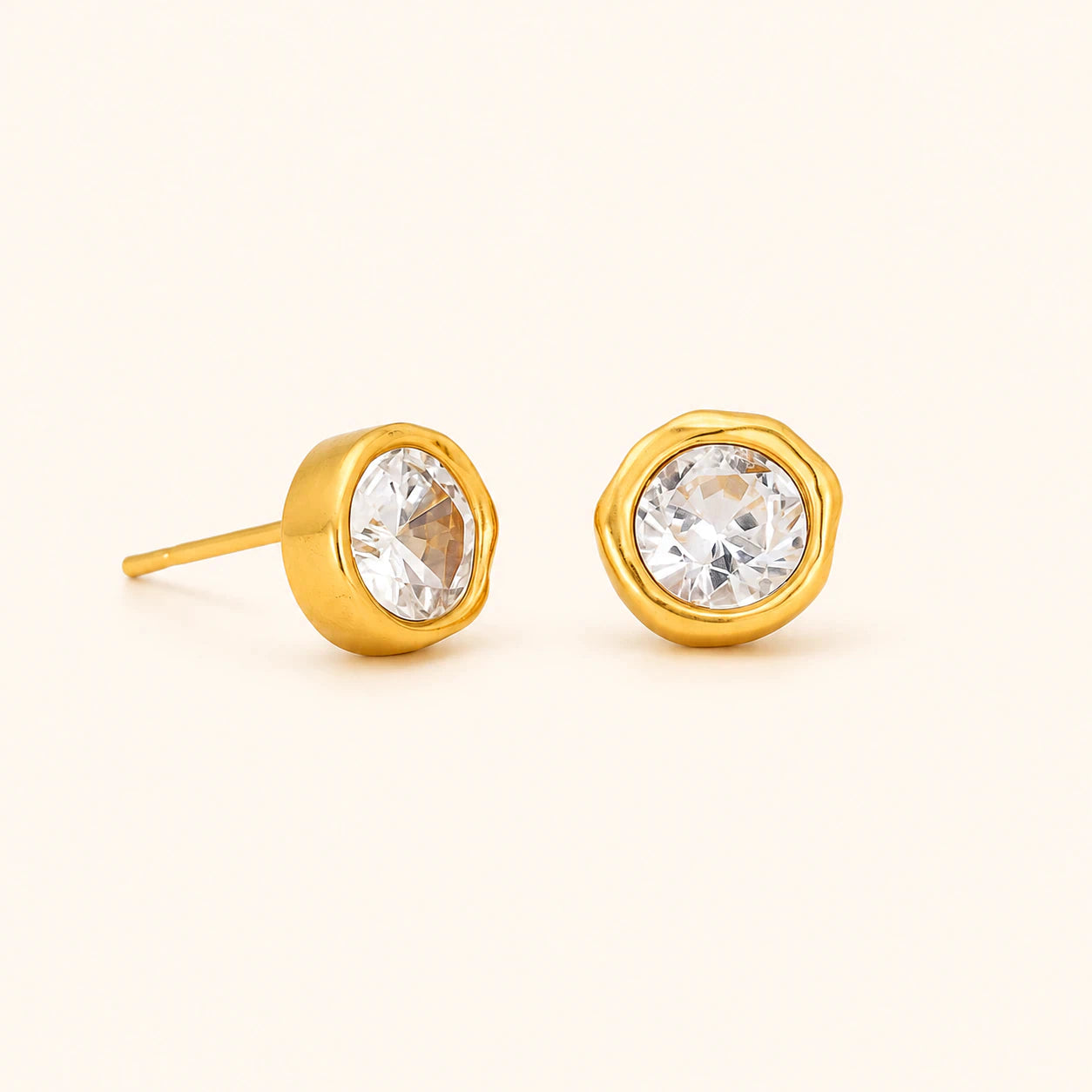 Gold stud earrings with clear gemstones on a beige background
