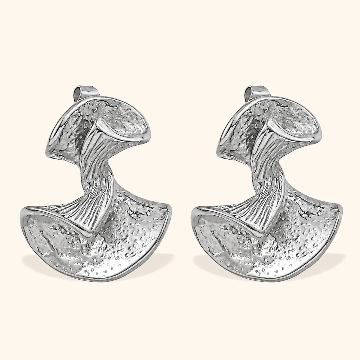 A pair of textured silver earrings with a sculptural, organic shape, displayed on a light cream background.