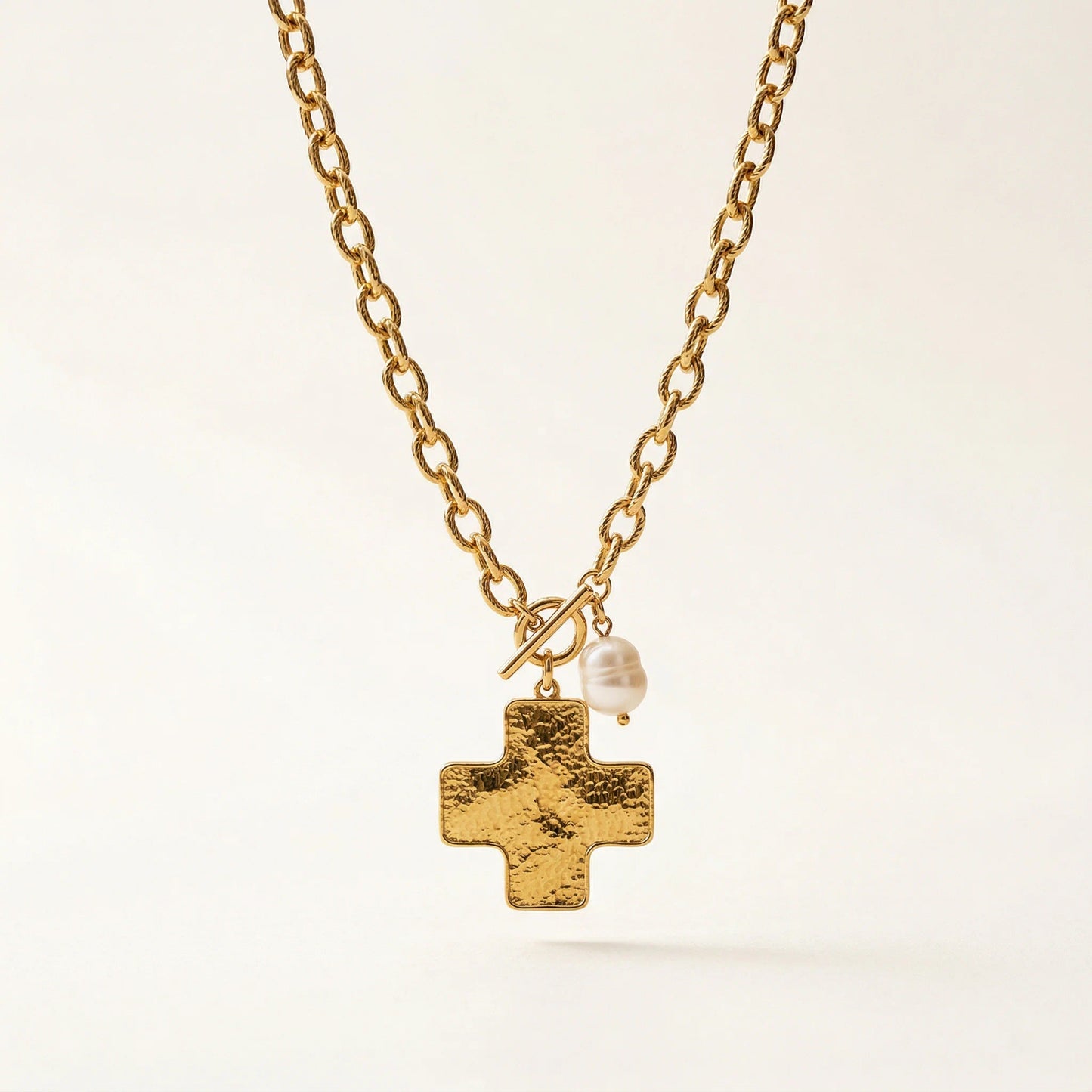 Gold necklace with a cross pendant and pearl on a light background