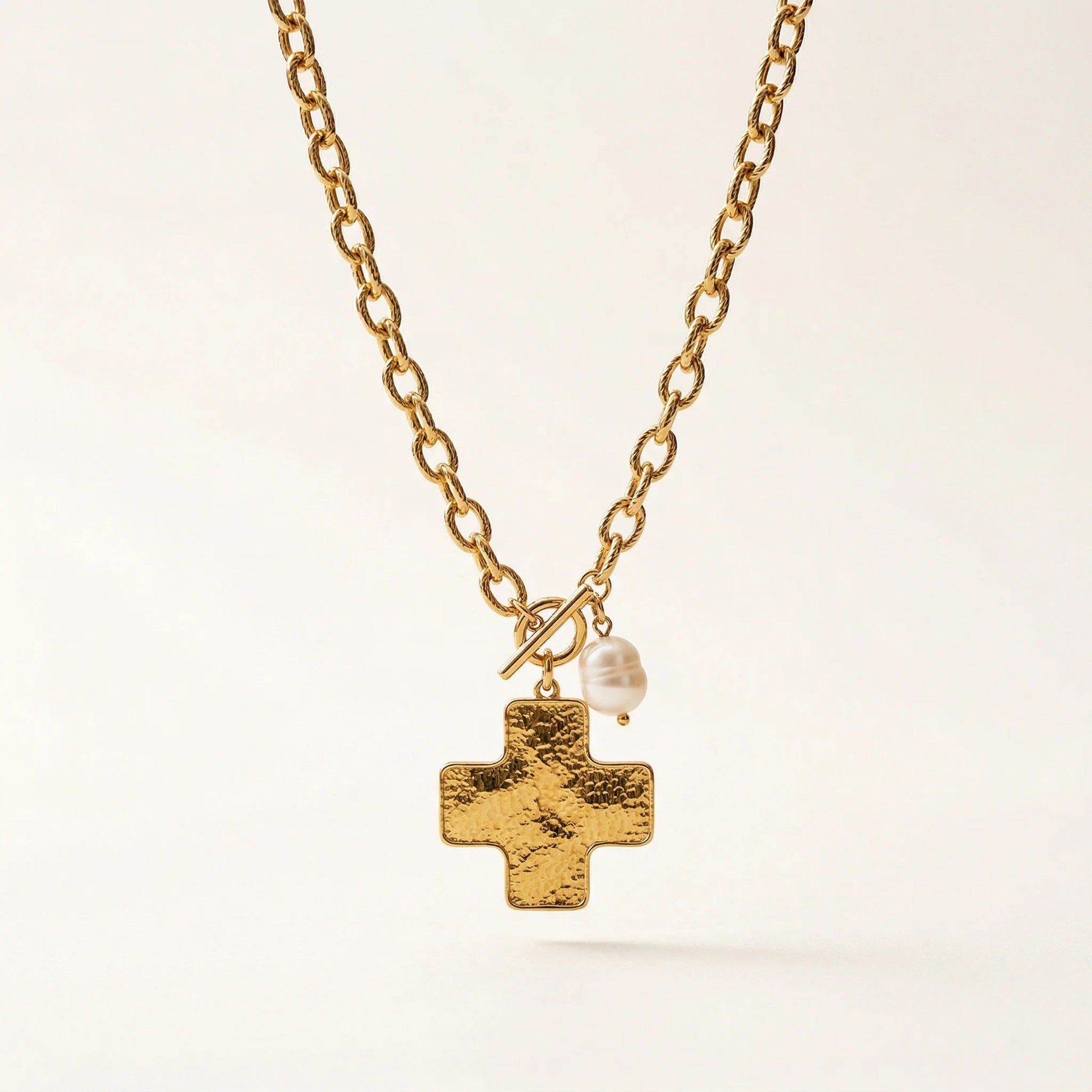Gold necklace with a cross pendant and pearl on a light background