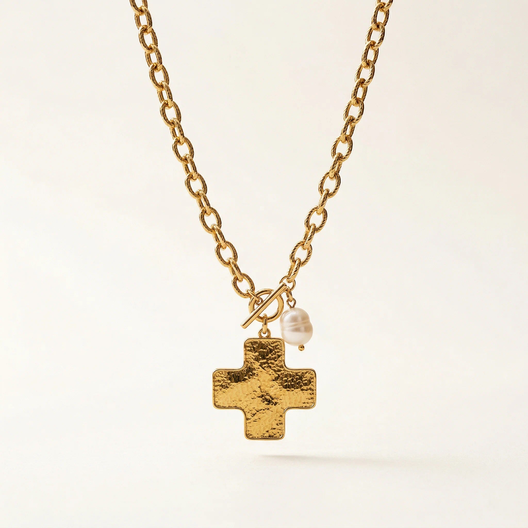 Gold necklace with a cross pendant and pearl on a light background