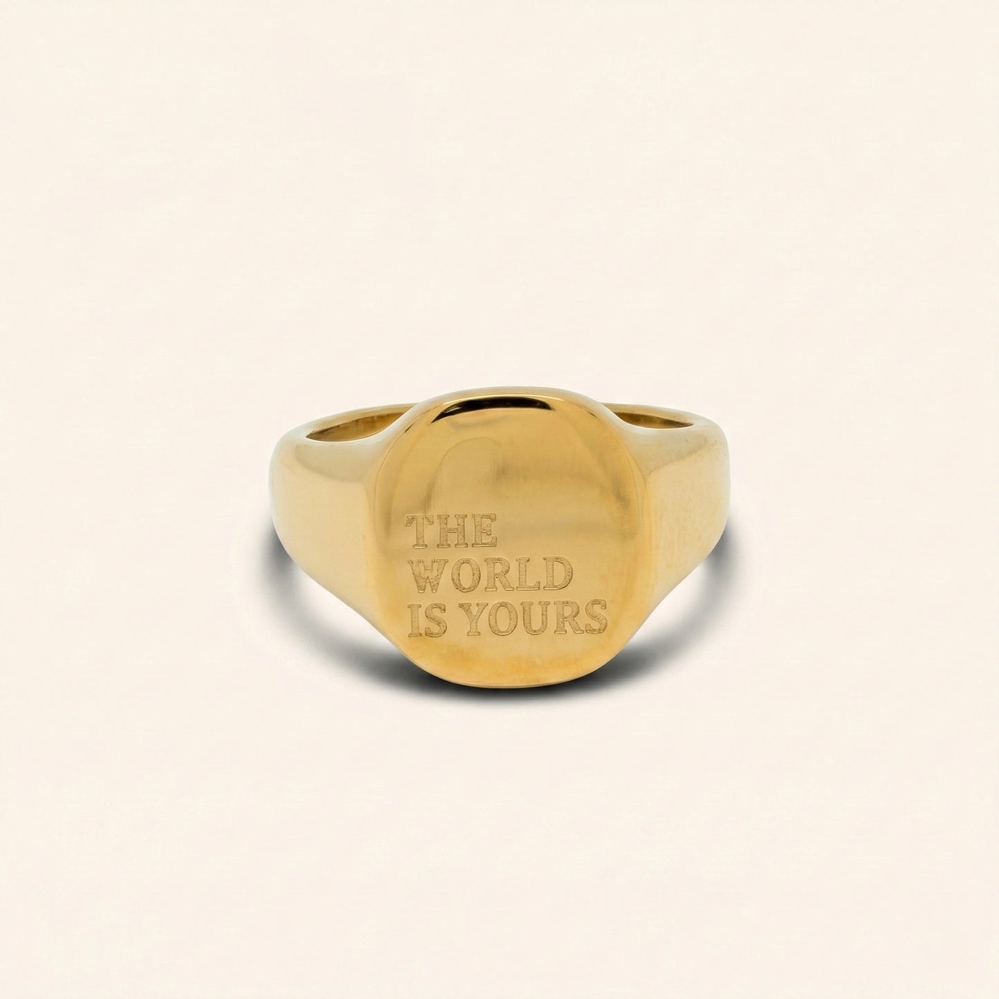 Gold ring with 'The World is Yours' engraving on a beige background