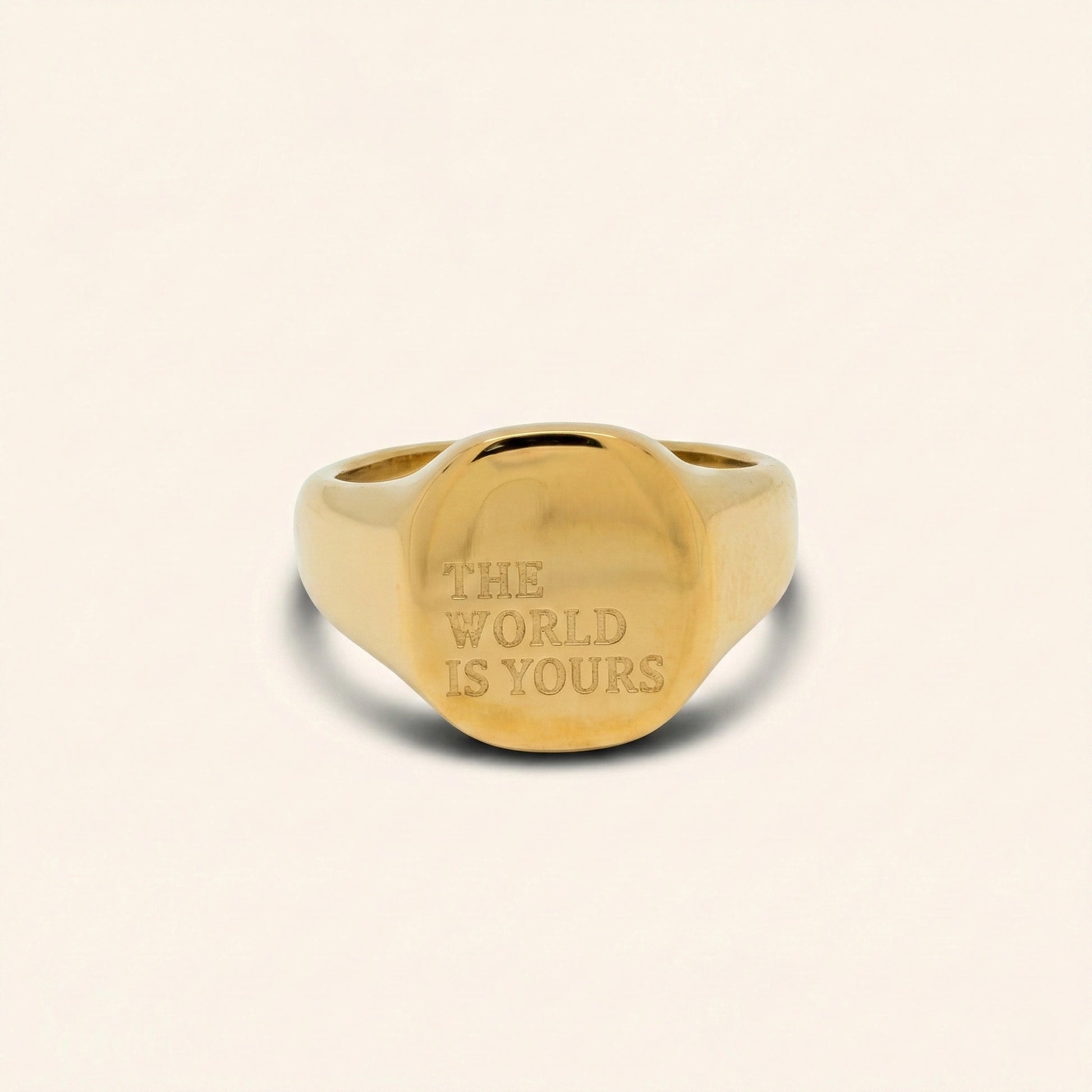 Gold ring with 'The World is Yours' engraving on a beige background