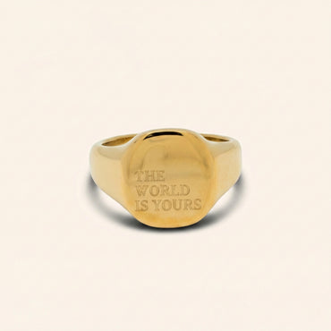 Gold ring with 'The World is Yours' engraving on a beige background