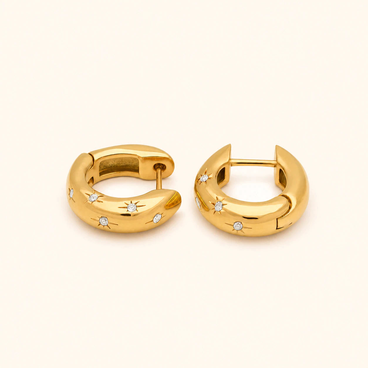 Pair of gold hoop earrings with small diamonds on a light beige background