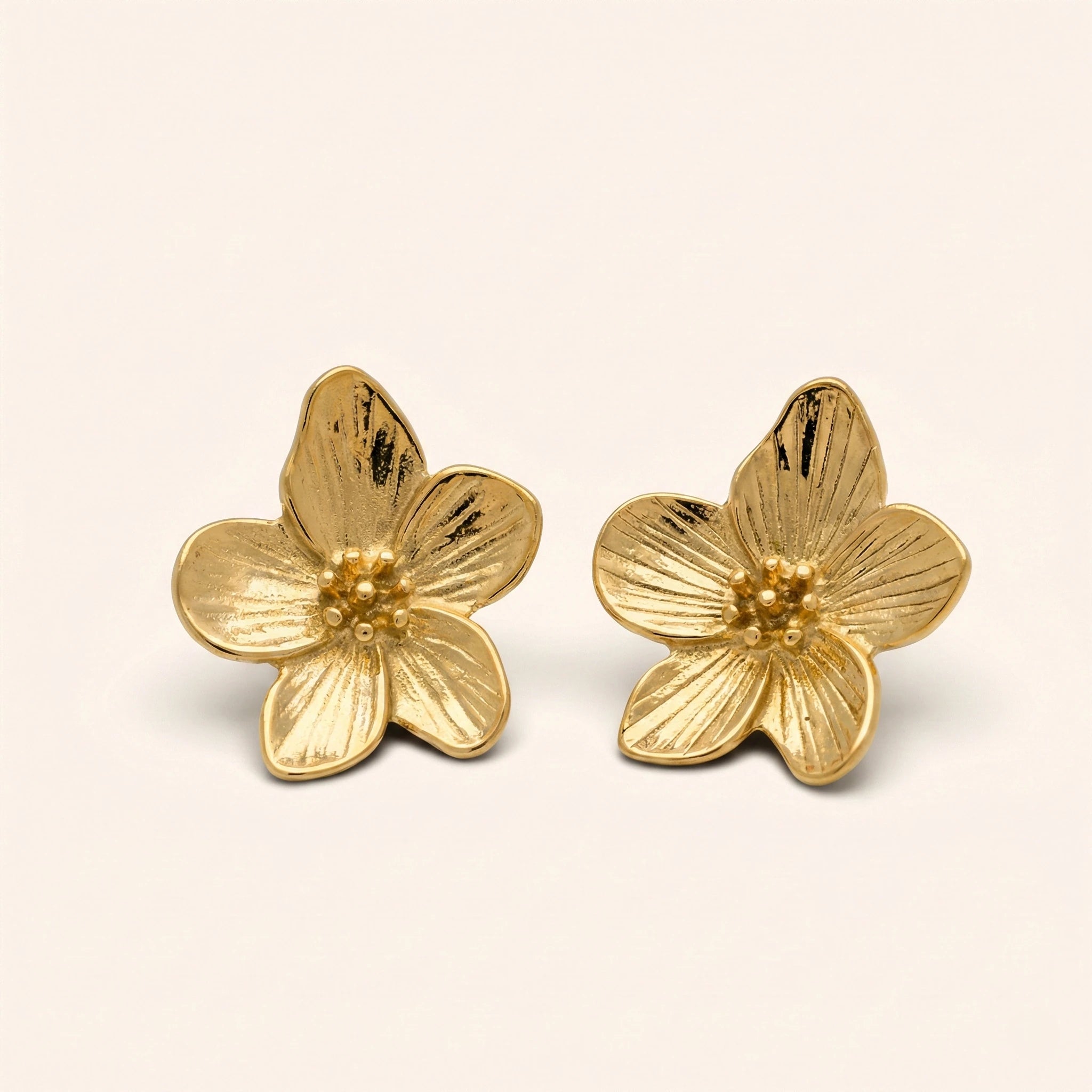 Gold flower-shaped earrings on a beige background