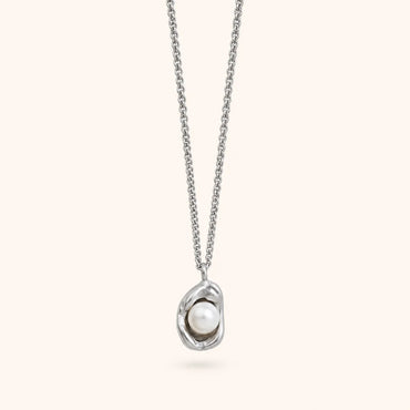 A silver chain necklace with an abstract, organic-shaped silver pendant holding a single white pearl, shown against a solid pale cream background.