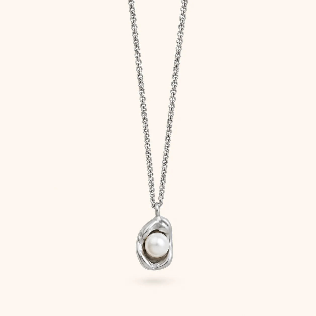 A silver chain necklace with an abstract, organic-shaped silver pendant holding a single white pearl, shown against a solid pale cream background.