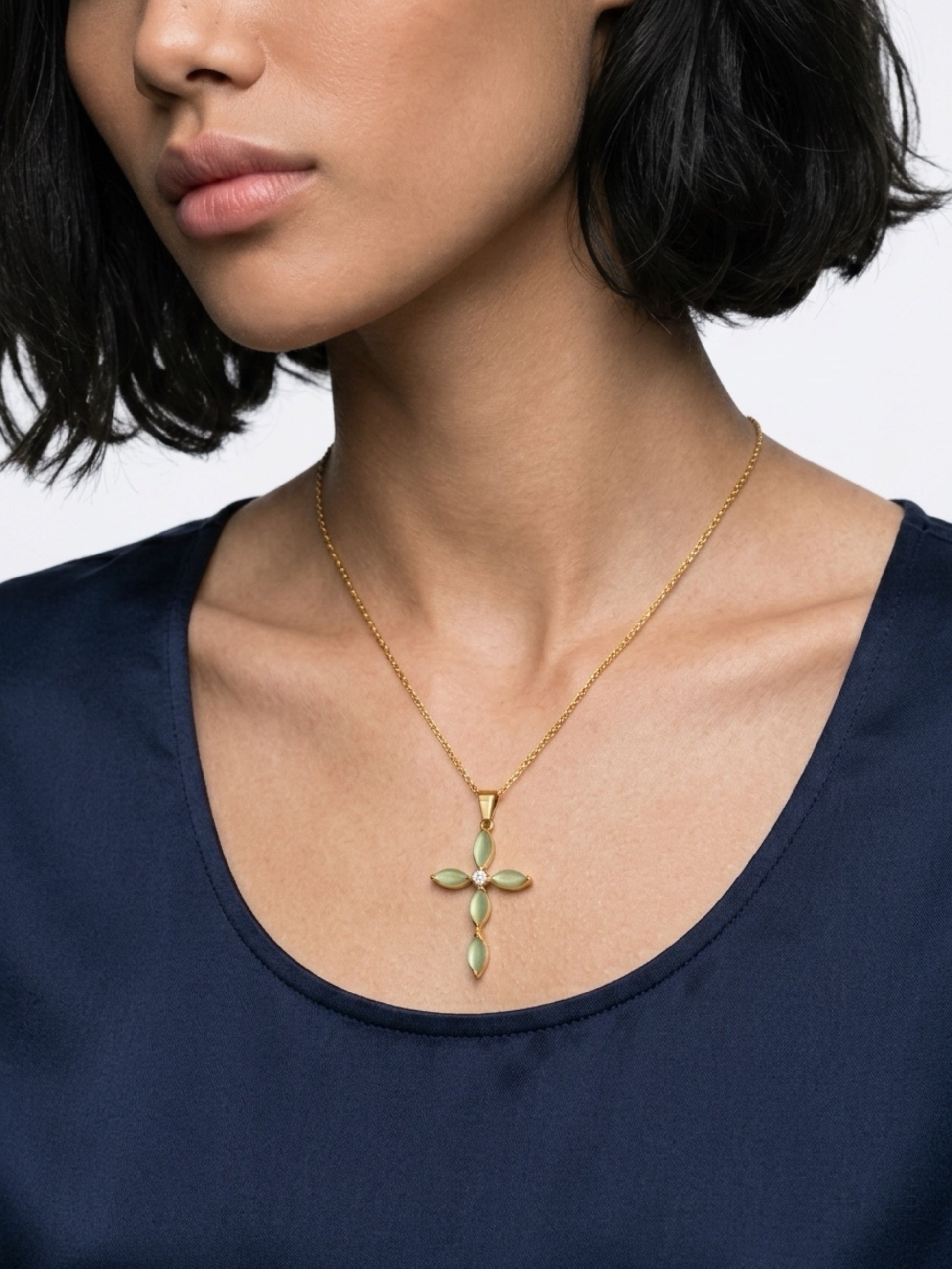 Woman wearing a gold necklace with a cross pendant on a plain background