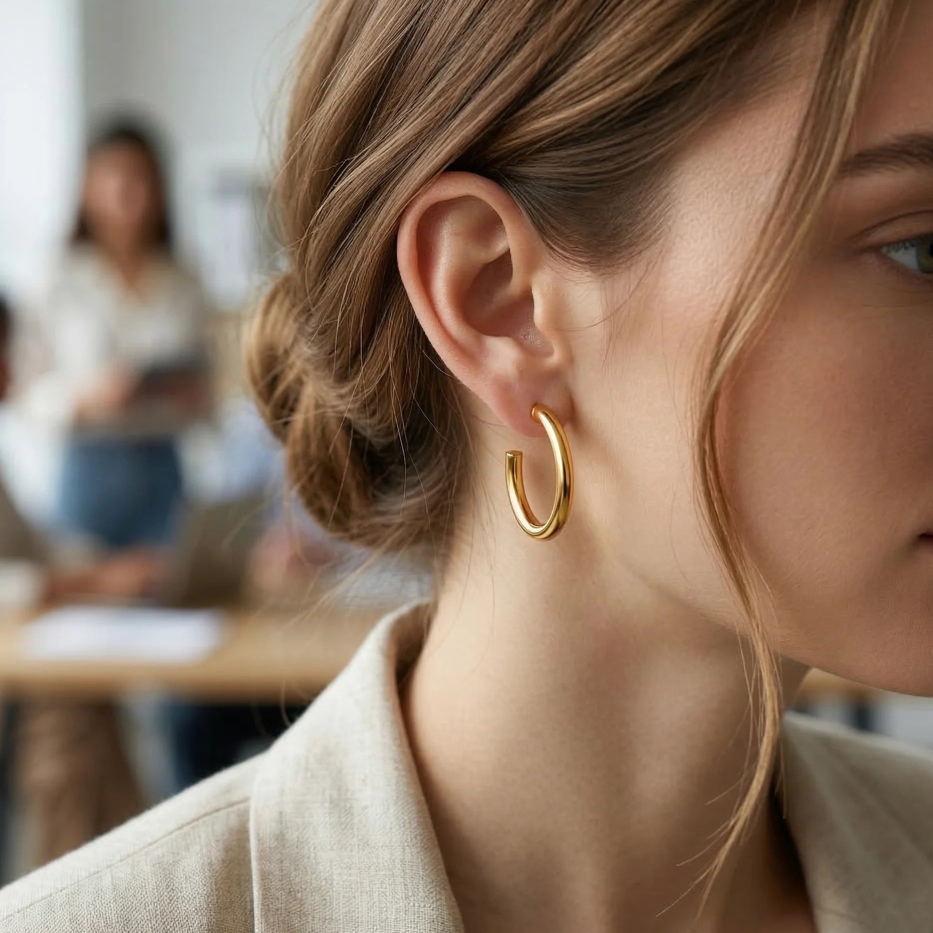 Close-up of a person wearing gold hoop earrings with a blurred background