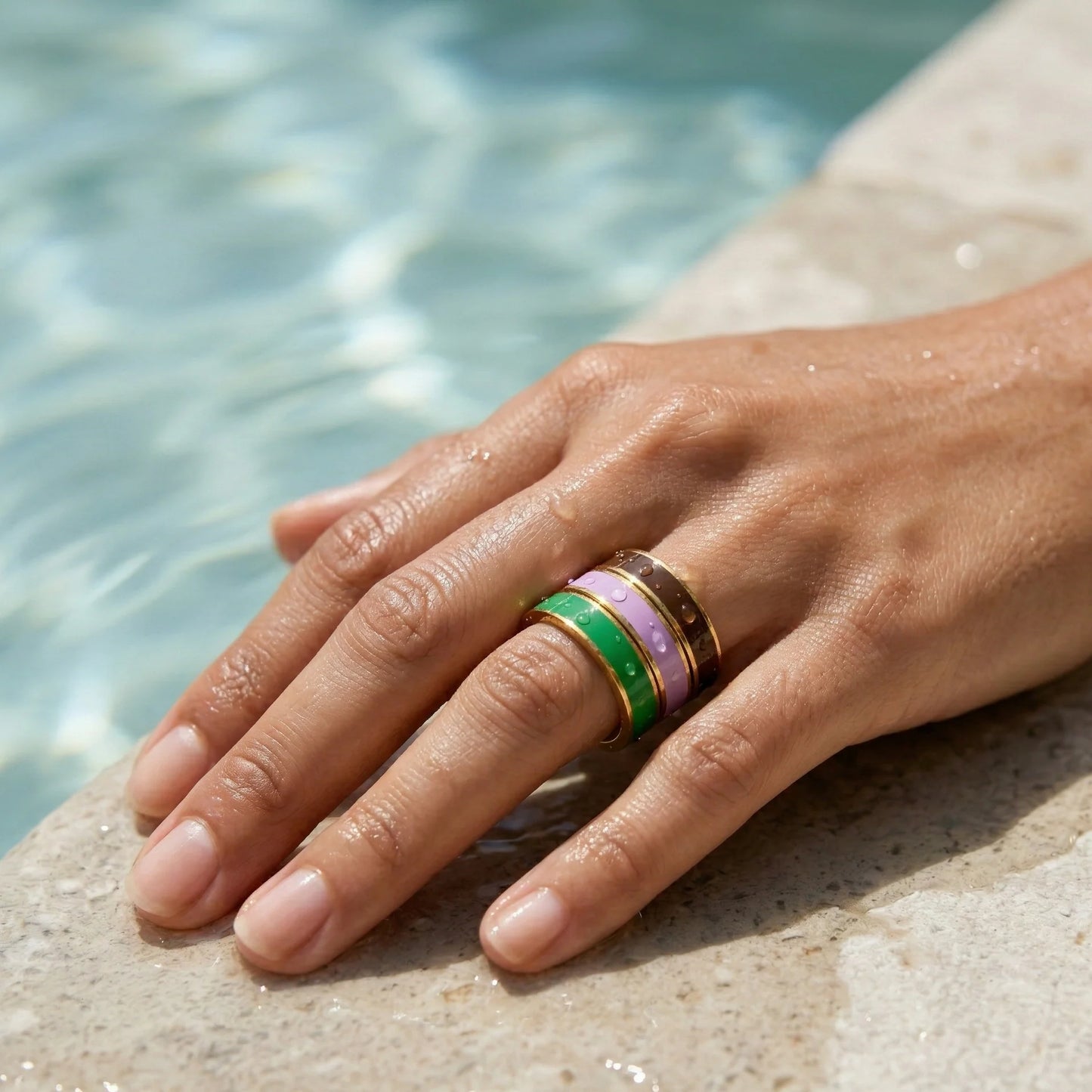 Hand wearing a ring with a green gemstone on a stone surface near water