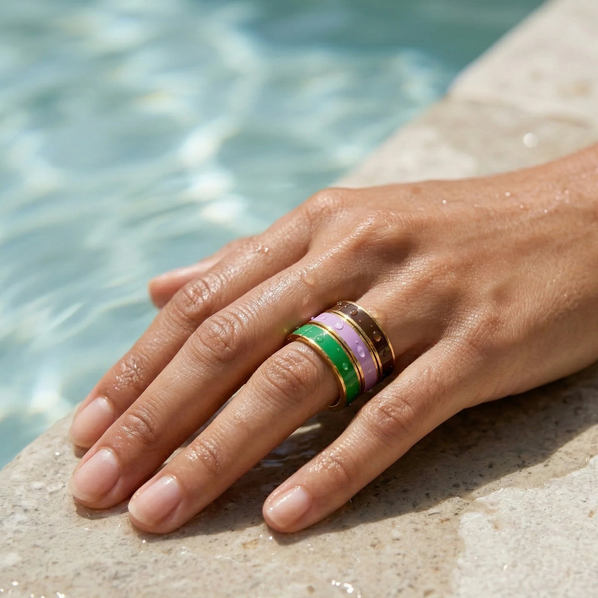 Hand wearing a ring with a green gemstone on a stone surface near water