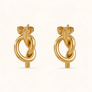 A pair of gold hoop earrings with a twisted knot design, shown on a clean off-white background.