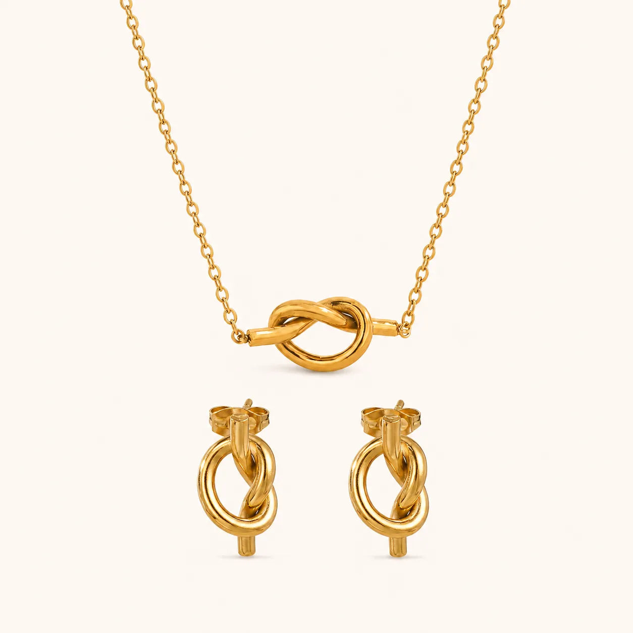 Gold jewelry set featuring a delicate chain necklace with a central knotted loop pendant and matching stud earrings with circular and knot details, displayed on a clean off-white background.