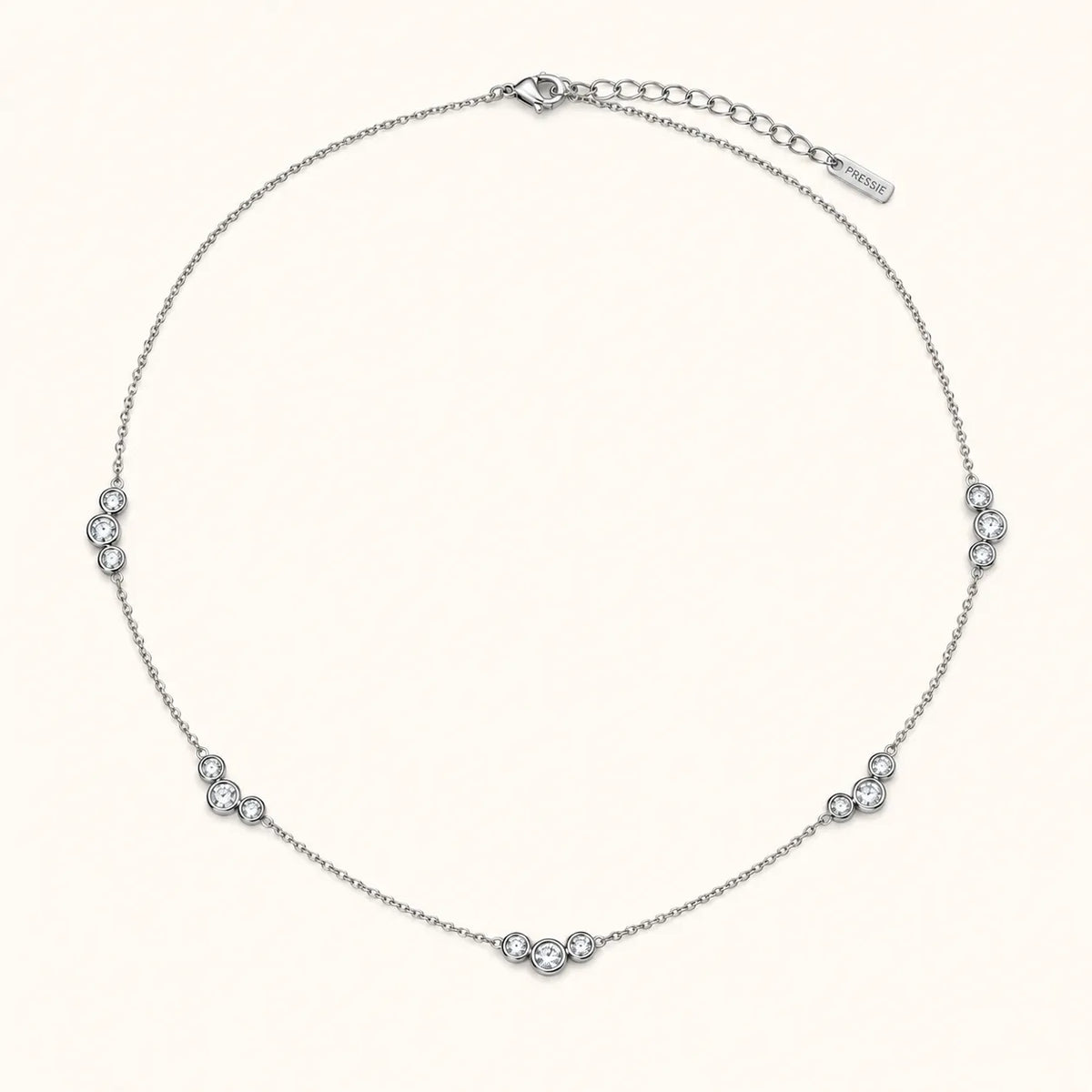 A delicate silver chain necklace with five small clusters of clear round-cut stones spaced evenly along the band, displayed on a light cream background. A brand tag is visible on the extender chain.