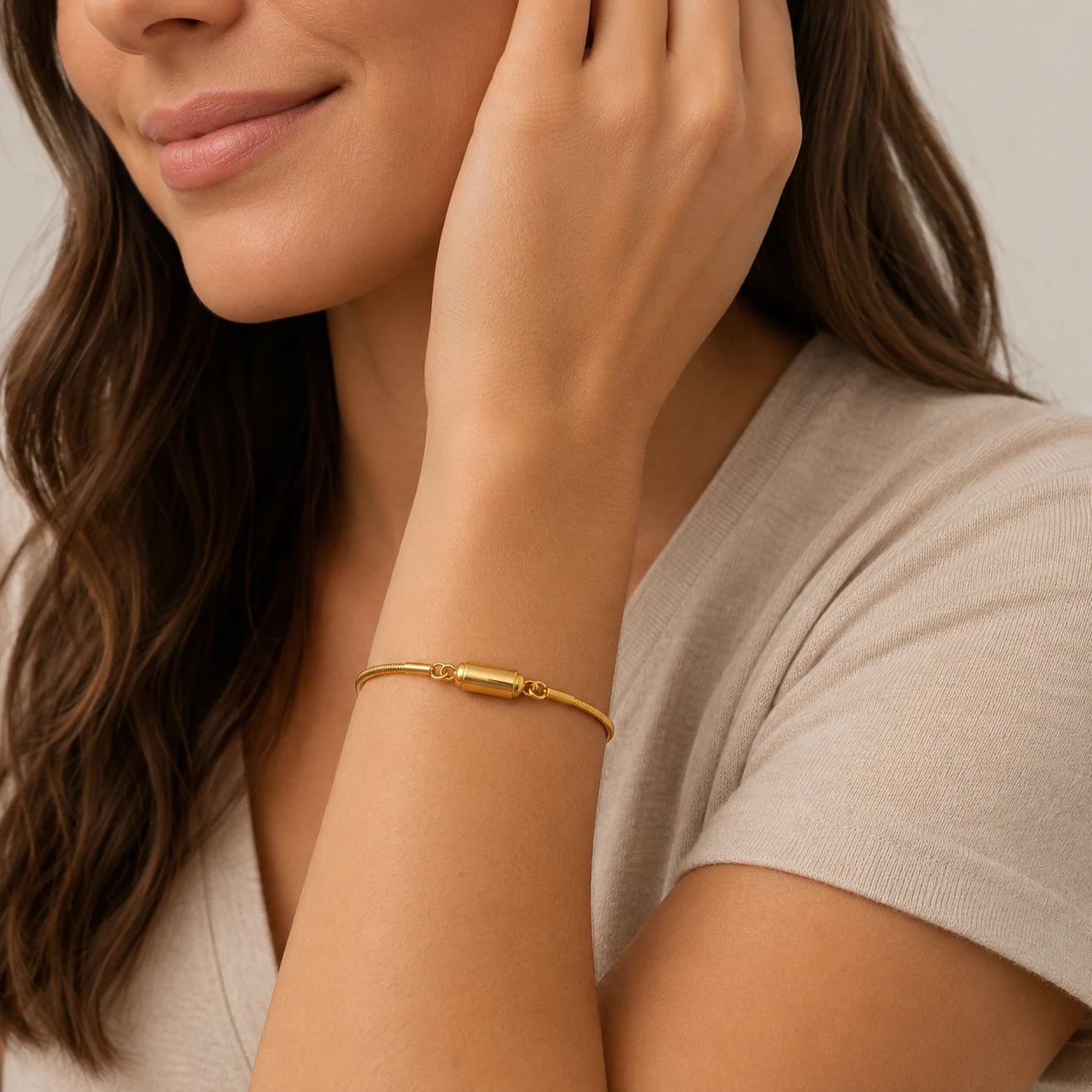 Woman wearing a gold bracelet on a neutral background