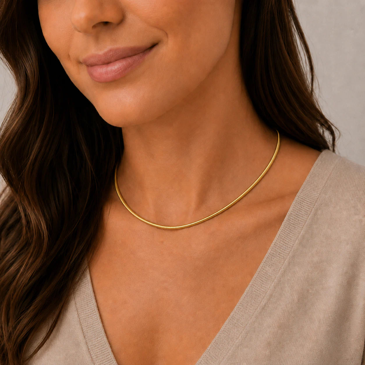 Woman wearing a gold necklace with a neutral background