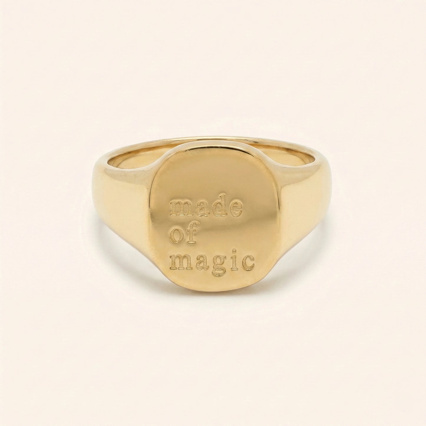 Gold ring with 'made of magic' engraving on a beige background