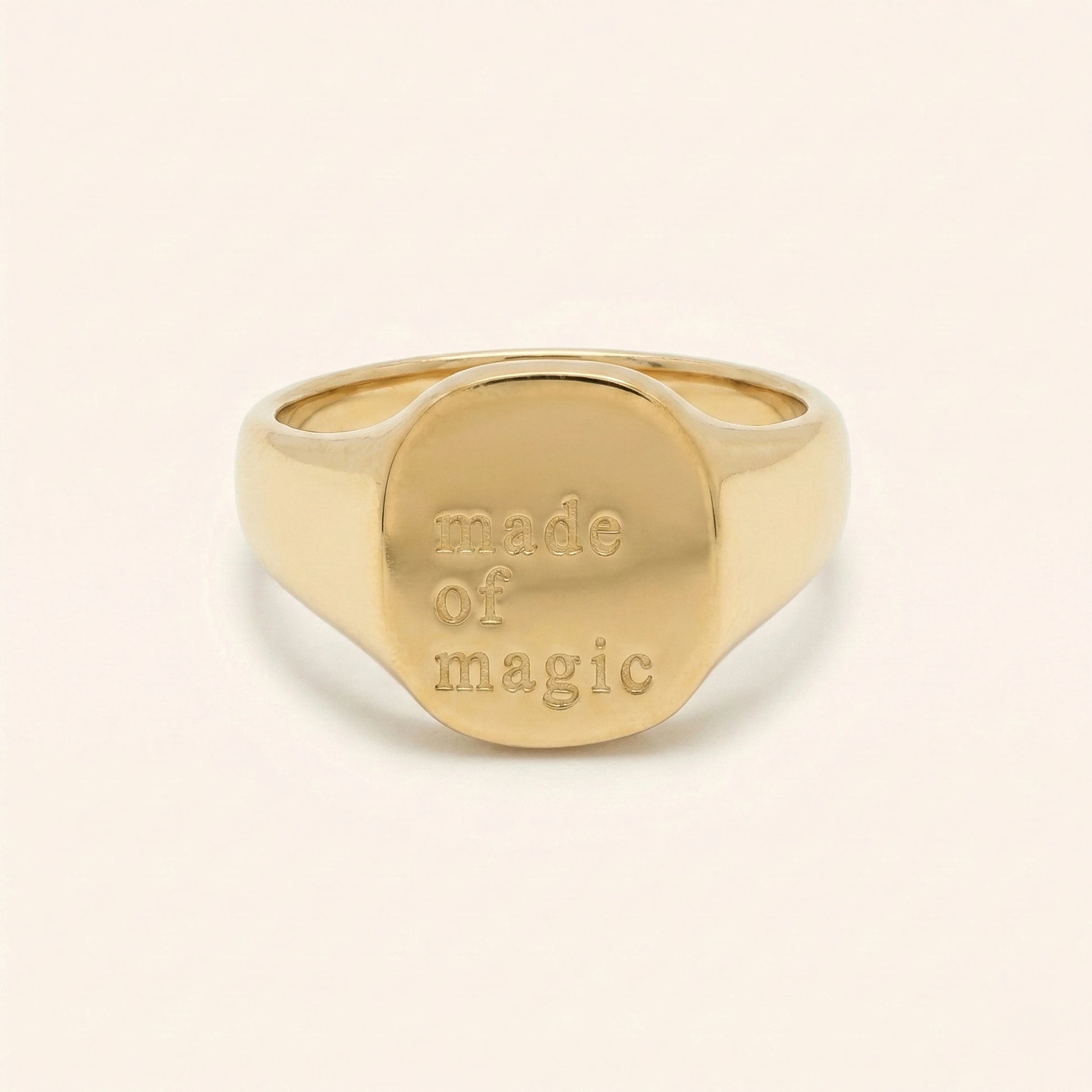 Gold ring with 'made of magic' engraving on a beige background