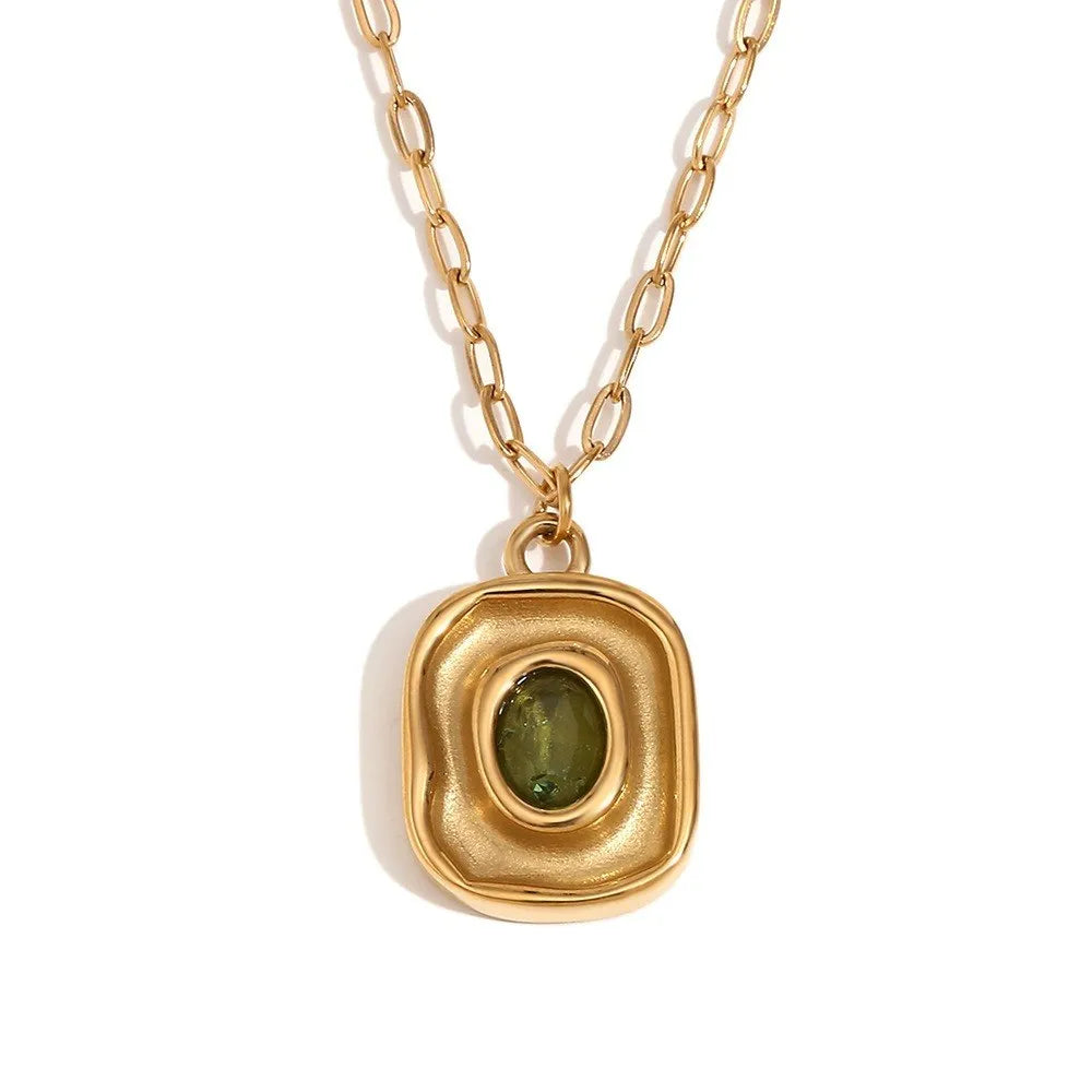 Gold necklace with a pendant featuring a green gemstone on a white background