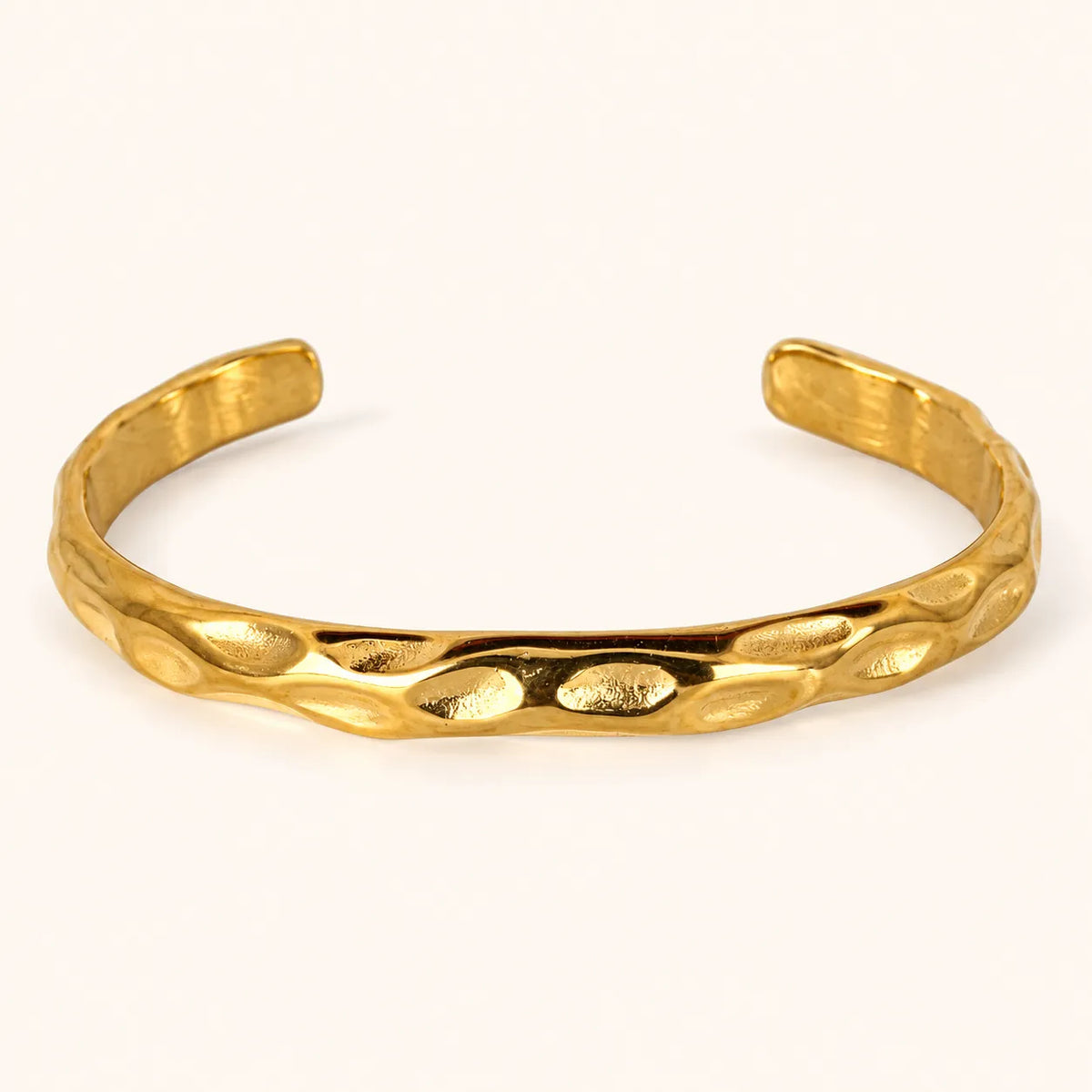 A textured gold cuff bracelet with a hammered, organic surface pattern, displayed on a clean off-white background.