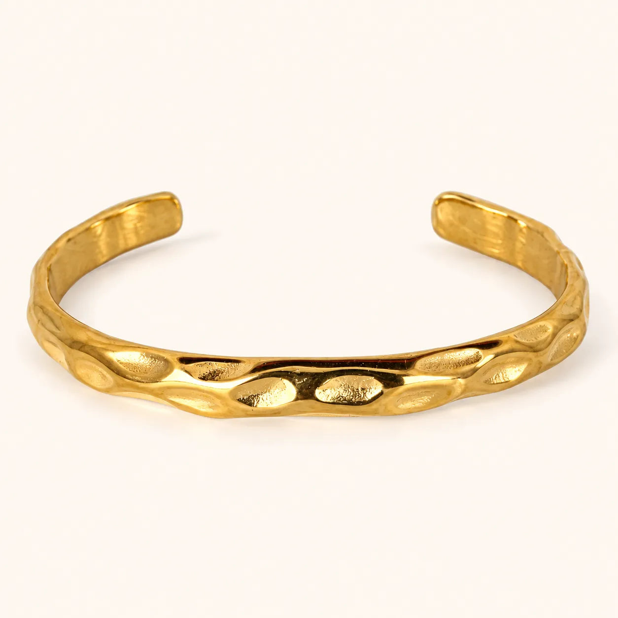 A textured gold cuff bracelet with a hammered, organic surface pattern, displayed on a clean off-white background.