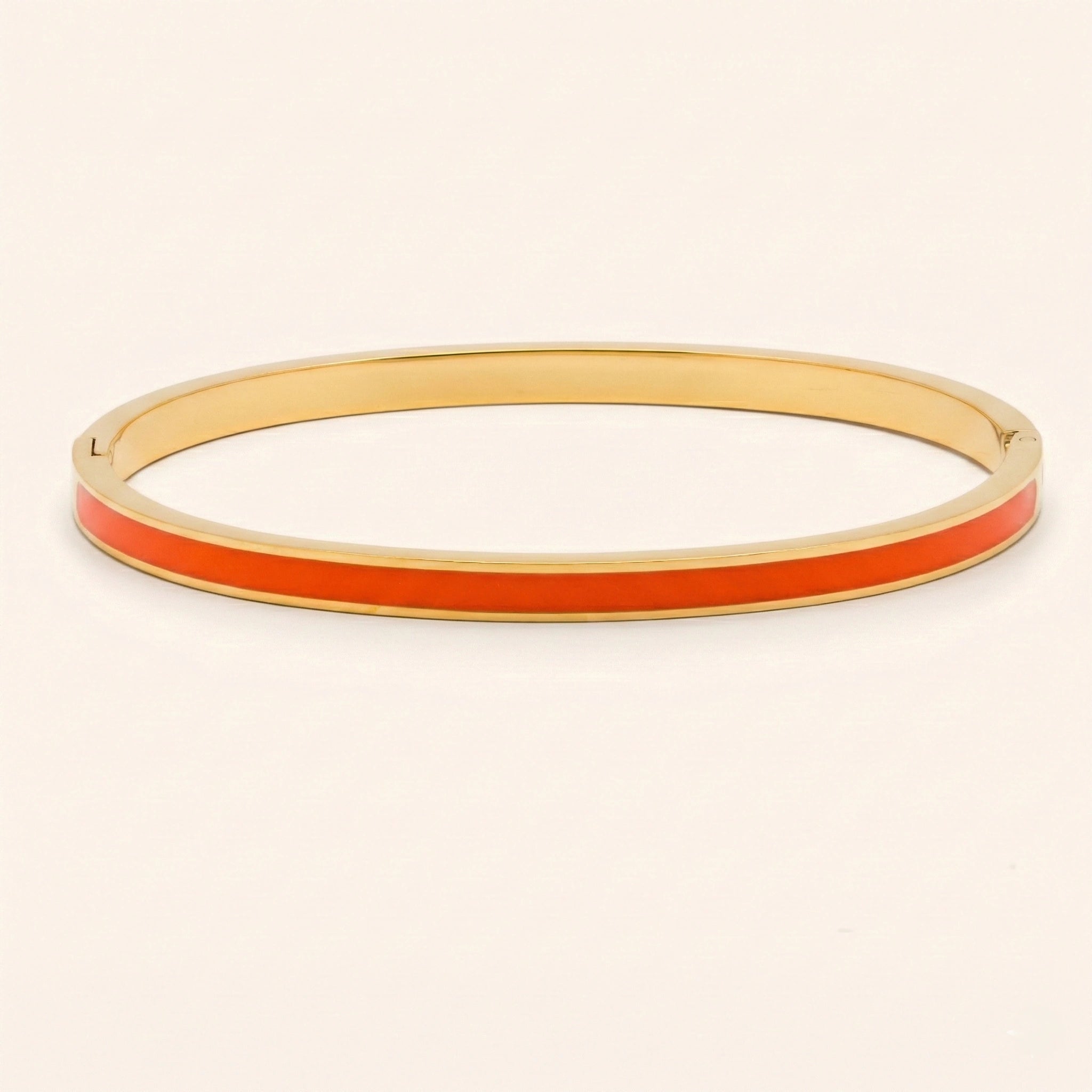 Gold bangle with a red-enamel band on a beige background