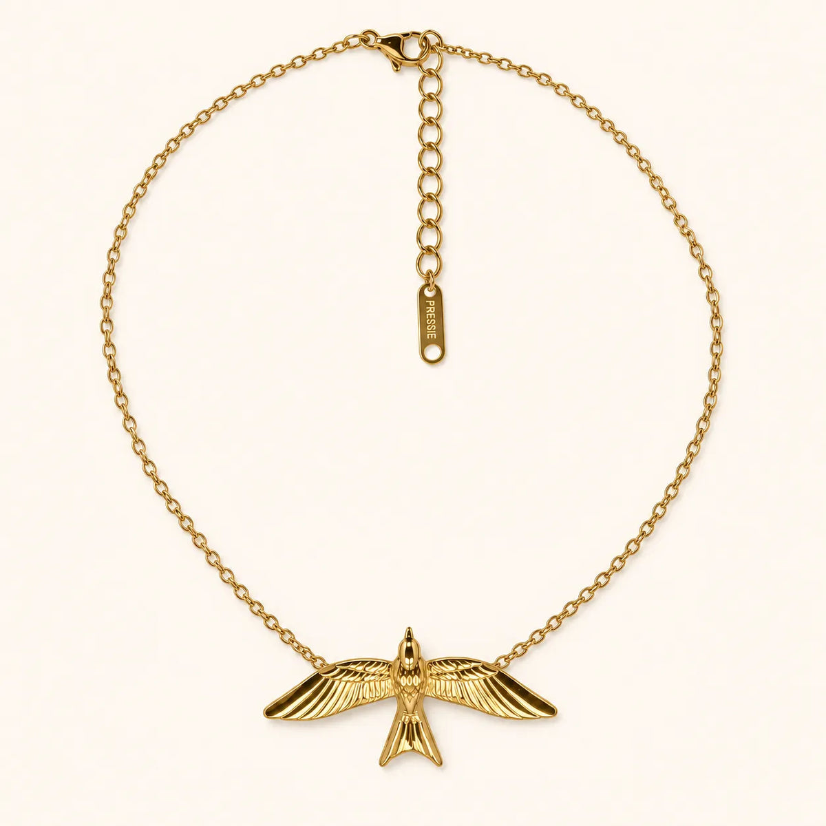 A gold chain necklace featuring a detailed bird pendant with spread wings, displayed on a clean off-white background. The necklace includes an extender chain with a small tag engraved with 'SUE' and a lobster clasp.