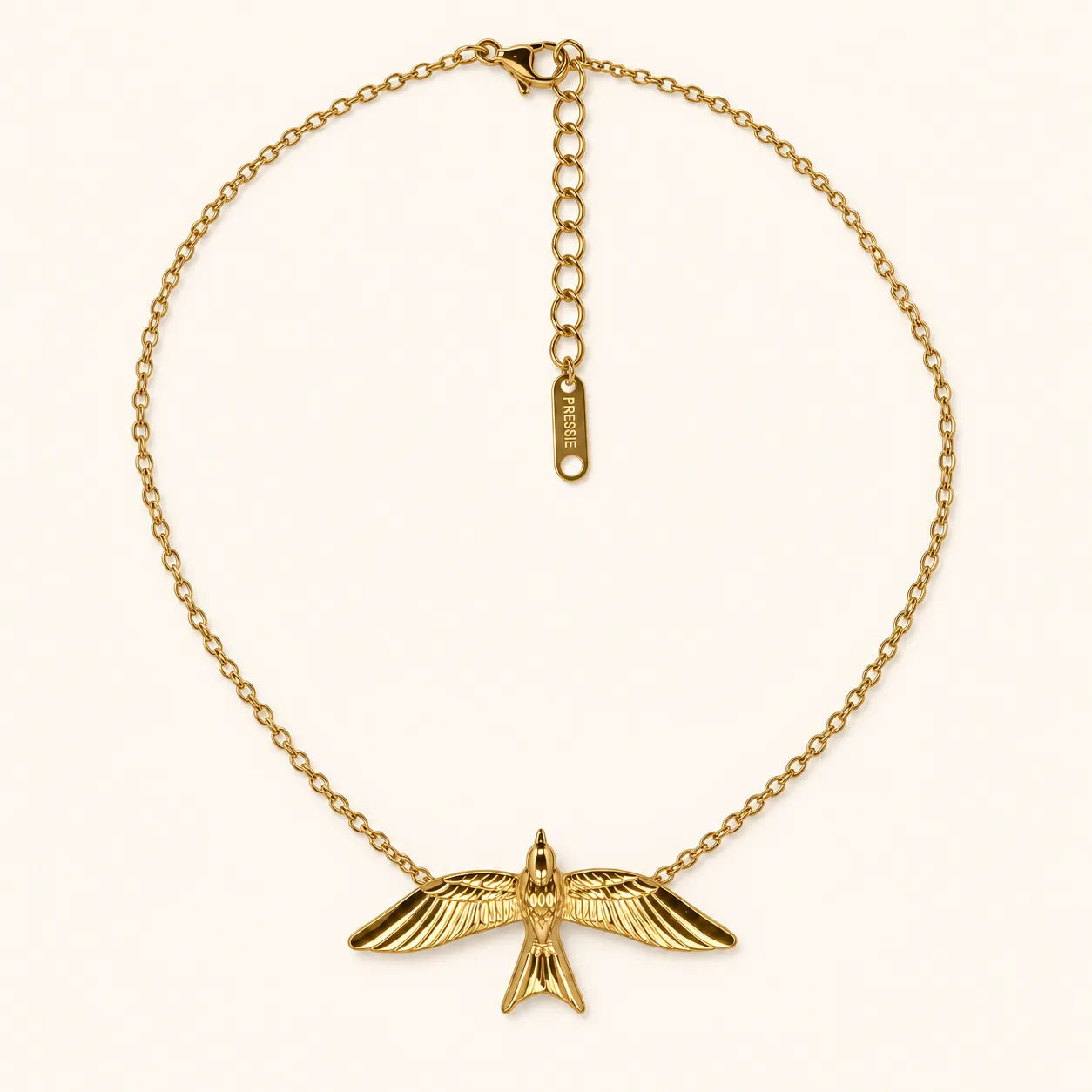 A gold chain necklace featuring a detailed bird pendant with spread wings, displayed on a clean off-white background. The necklace includes an extender chain with a small tag engraved with 'SUE' and a lobster clasp.