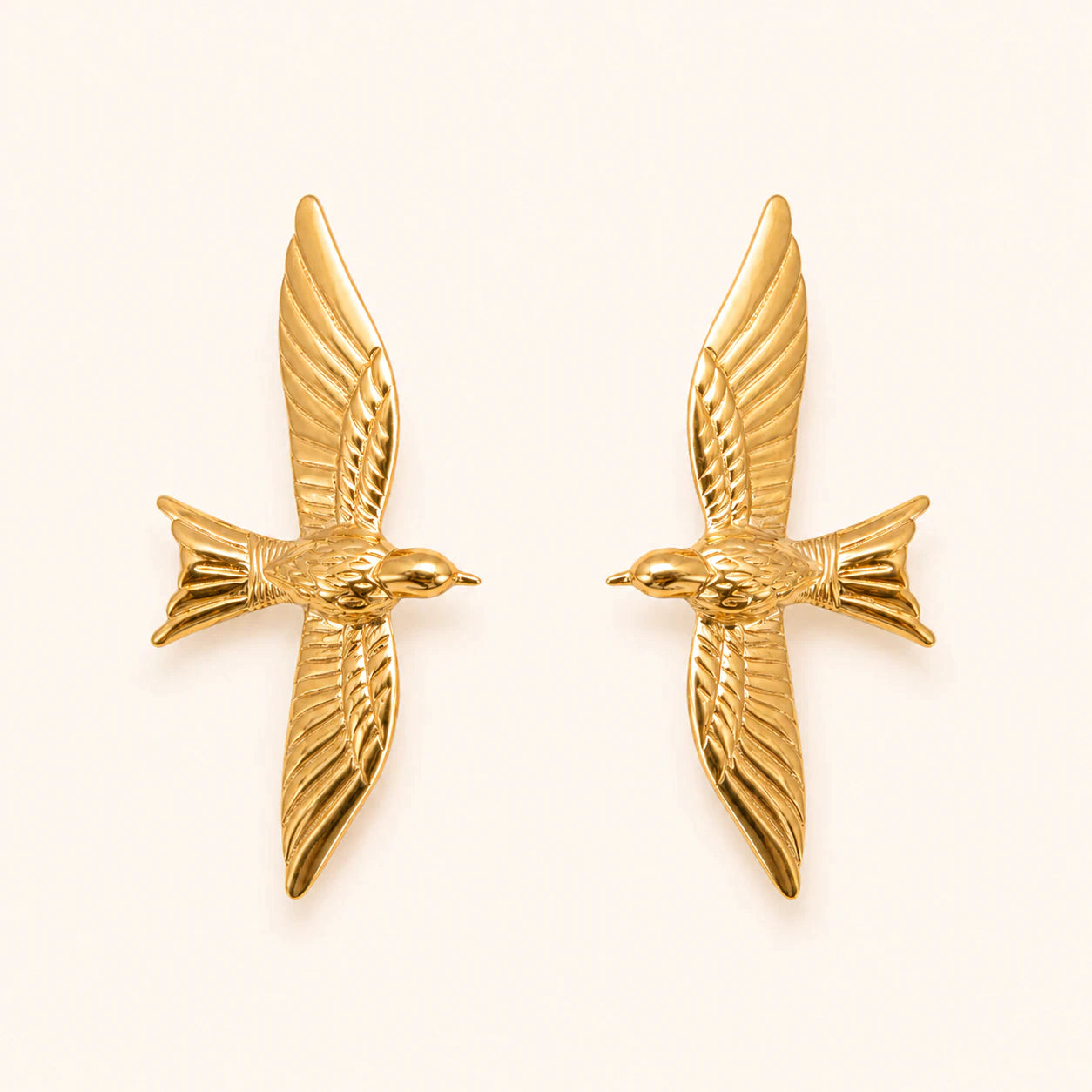 Pair of gold bird-shaped earrings on a light beige background