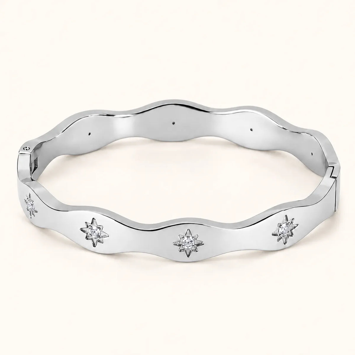 A polished silver-tone wavy bangle bracelet with three starburst motifs set with clear stones, displayed on a light cream background.