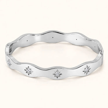 A polished silver-tone wavy bangle bracelet with three starburst motifs set with clear stones, displayed on a light cream background.