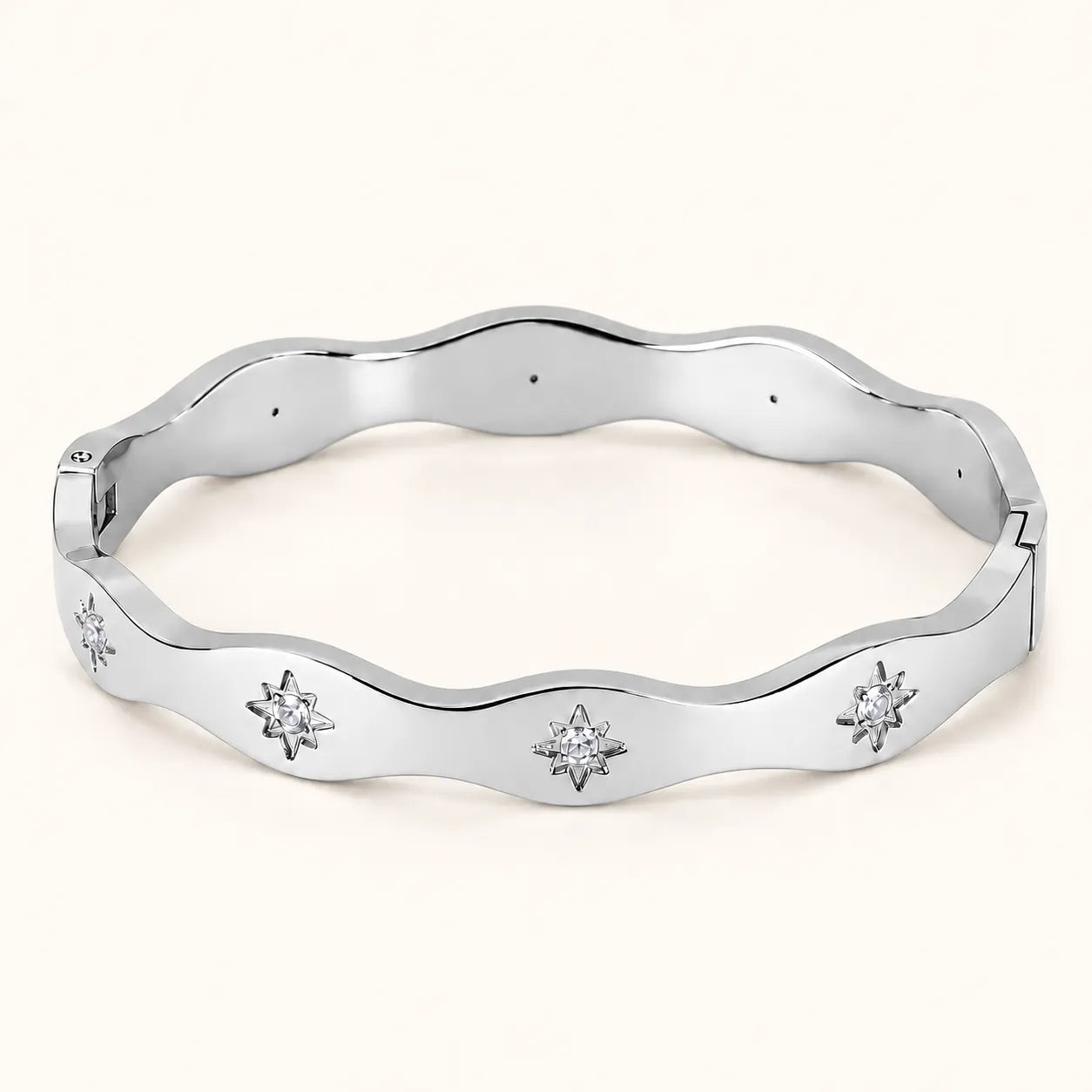 A polished silver-tone wavy bangle bracelet with three starburst motifs set with clear stones, displayed on a light cream background.