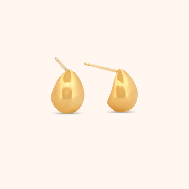 Close-up of gold teardrop earrings, showcasing their smooth, polished surface and modern, sculptural design.
